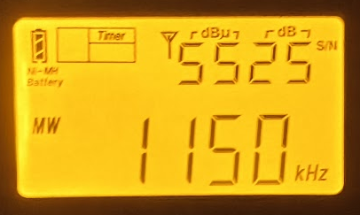 Foto do display do receptor Tecsun PL-398BT sintonizado em AM 1150 kHz às 18:49, marcando 55 dBμ e 25 dB S/N. O led âmbar de seu display está ligado.